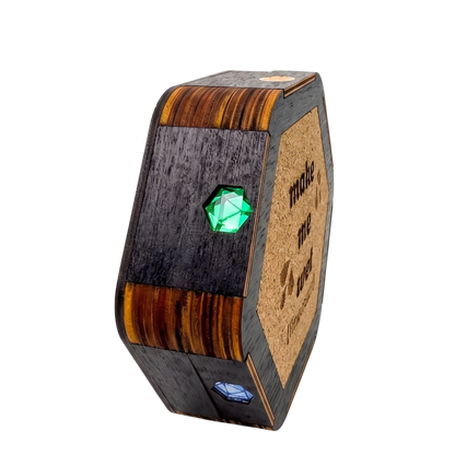Closed Jeweled Agenda Dice Vault on its side showing the layered birch edge, green and blue mirrored D20 pride gems, and the cork make me wet coaster base